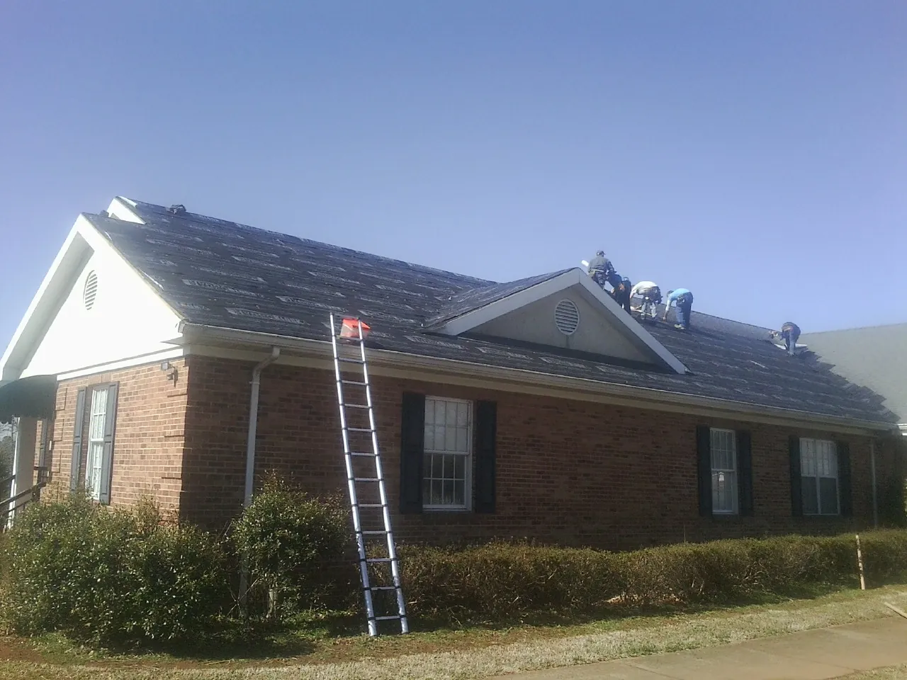 Crew tearing shingles off a brick ranch roof with a ladder set — Metal Roof Repair work by our crew in Maryville