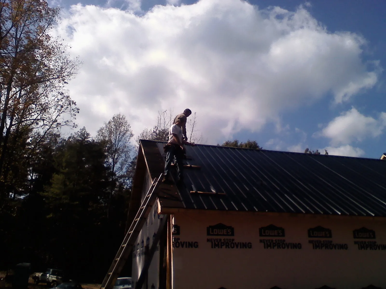 Roofer fastening dark metal panels high against a cloudy sky, from a Roof Inspection job in Maryville