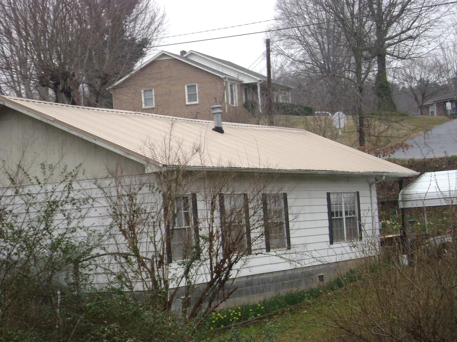 Tan metal roof on a white sided house set into a hillside — Commercial Roofing by Roofing Brothers in Maryville