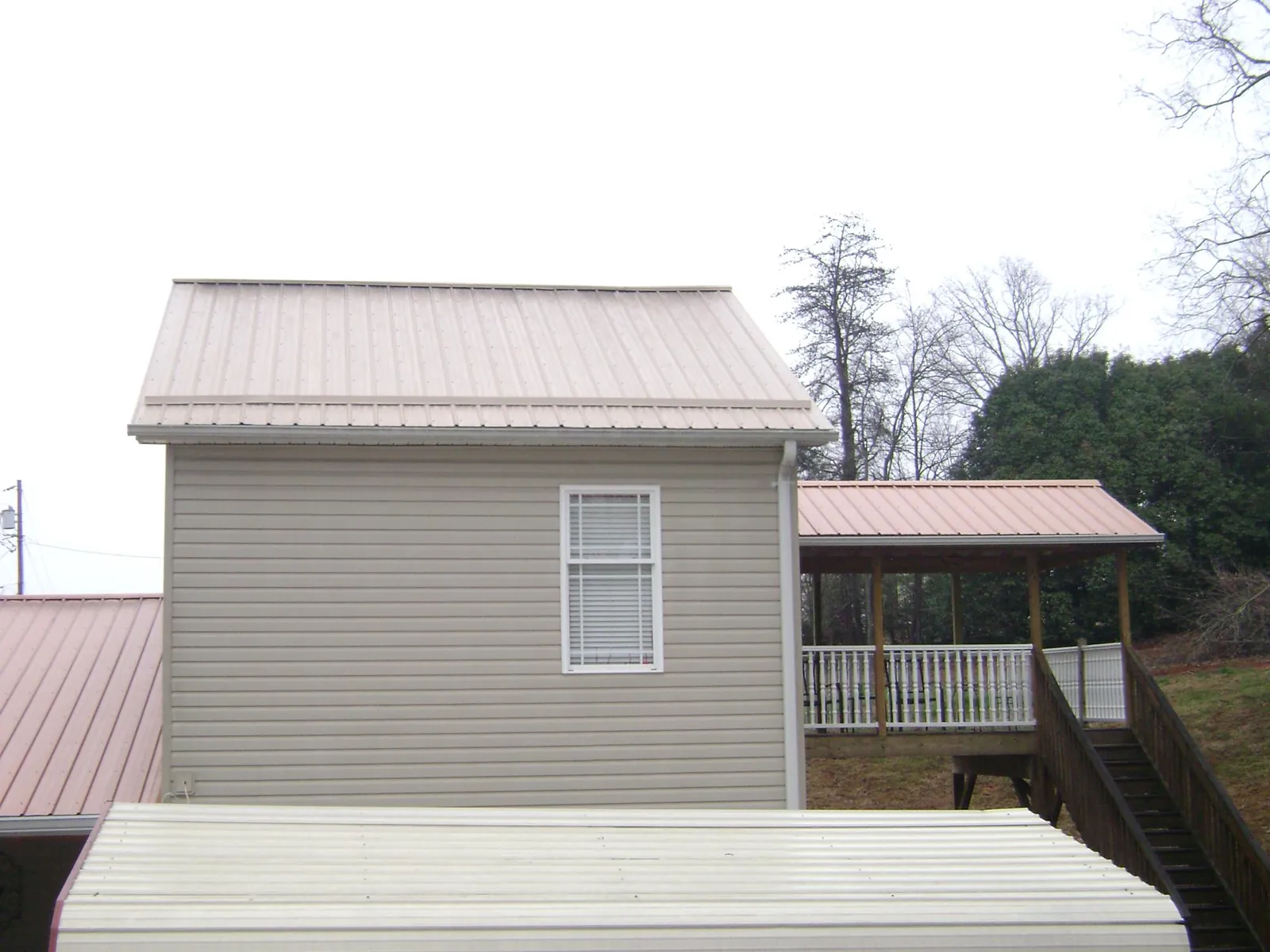 Tan metal roofs on a two story addition and attached porch, from a Roof Replacement job in Maryville